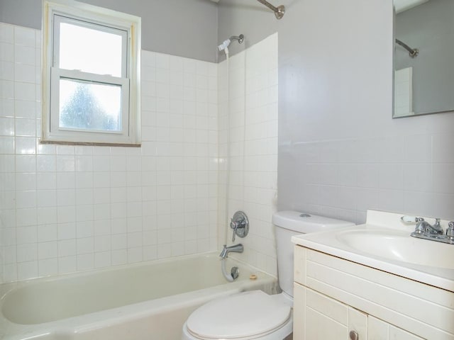 full bathroom featuring tiled shower / bath, vanity, tile walls, and toilet