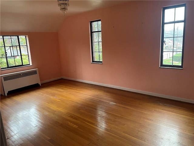 unfurnished room with radiator heating unit, light wood-type flooring, vaulted ceiling, and a notable chandelier