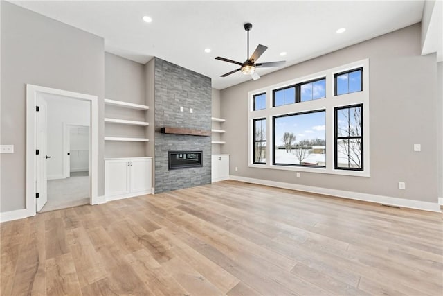 unfurnished living room featuring a fireplace, built in shelves, light hardwood / wood-style flooring, and ceiling fan