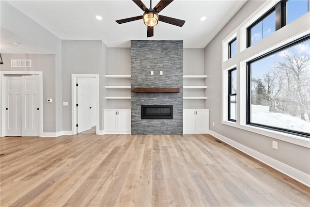 unfurnished living room featuring a stone fireplace, ceiling fan, built in shelves, and light hardwood / wood-style floors