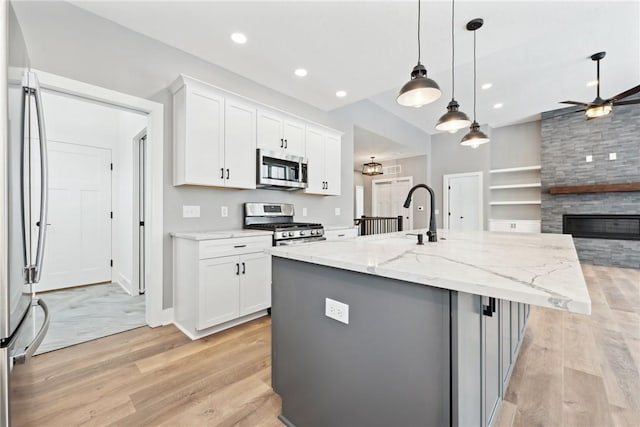 kitchen featuring a kitchen island with sink, white cabinets, light stone countertops, and appliances with stainless steel finishes