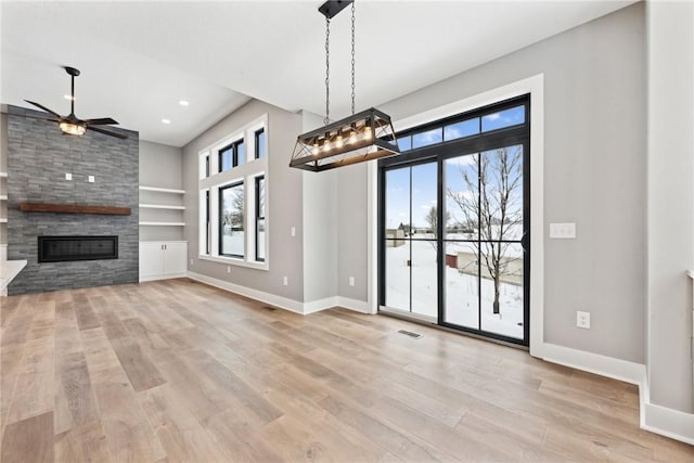 unfurnished living room with built in shelves, ceiling fan, a fireplace, and light wood-type flooring