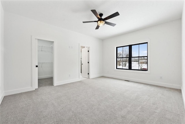 unfurnished bedroom featuring light carpet, a closet, a spacious closet, and ceiling fan