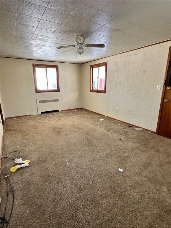 carpeted empty room with plenty of natural light, radiator, and ceiling fan