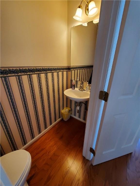 bathroom with toilet, hardwood / wood-style floors, and an inviting chandelier