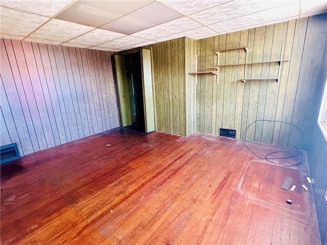 unfurnished room with a drop ceiling and wooden walls