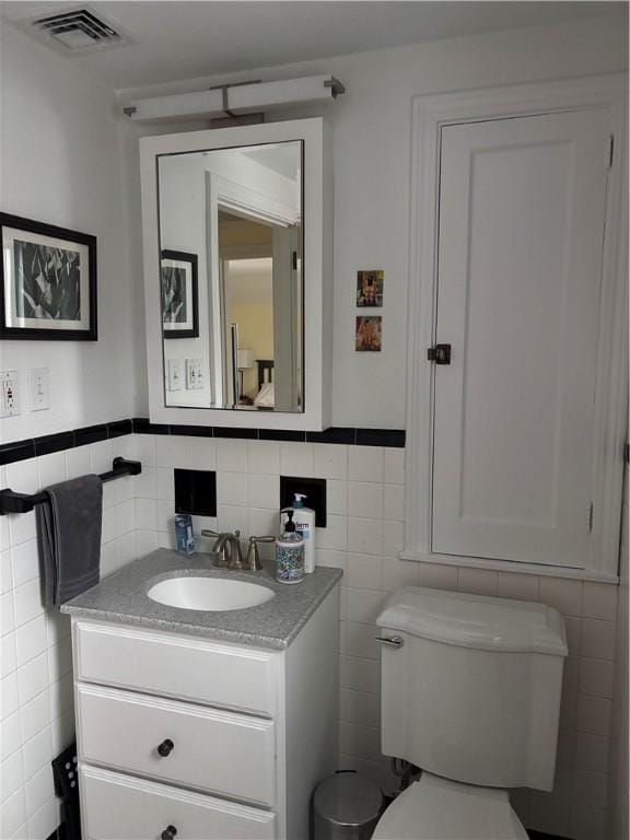 bathroom featuring toilet, vanity, and tile walls