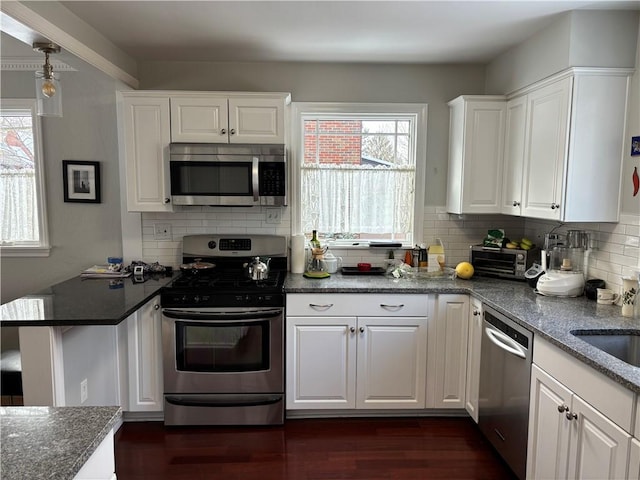 kitchen featuring dark stone counters, appliances with stainless steel finishes, backsplash, and white cabinetry