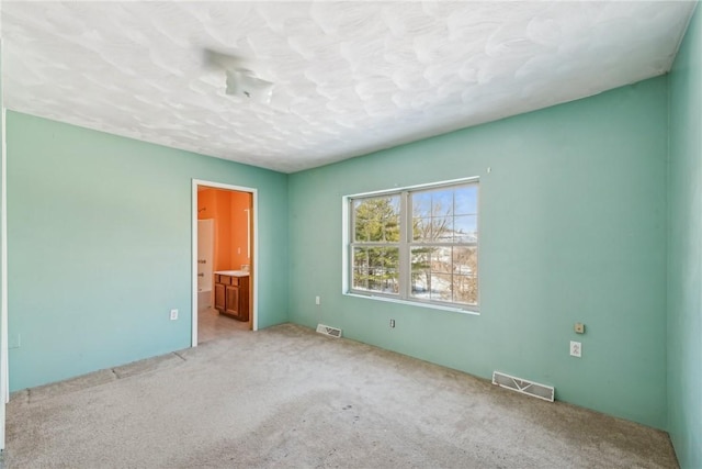 unfurnished bedroom with a textured ceiling, light colored carpet, and ensuite bath