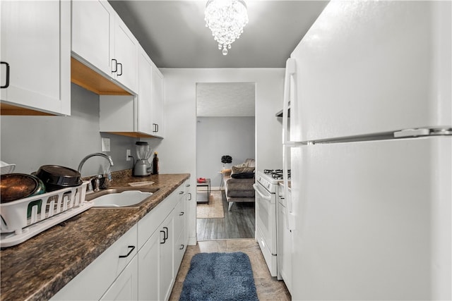 kitchen featuring white appliances, dark stone counters, white cabinets, sink, and a chandelier