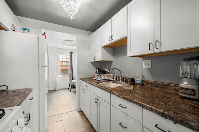 kitchen with white cabinets, white fridge, dark stone countertops, and sink