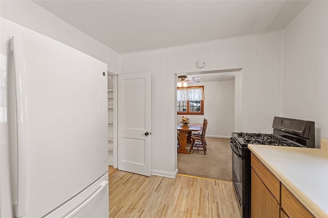 kitchen with ceiling fan, white refrigerator, light wood-type flooring, and black gas range oven