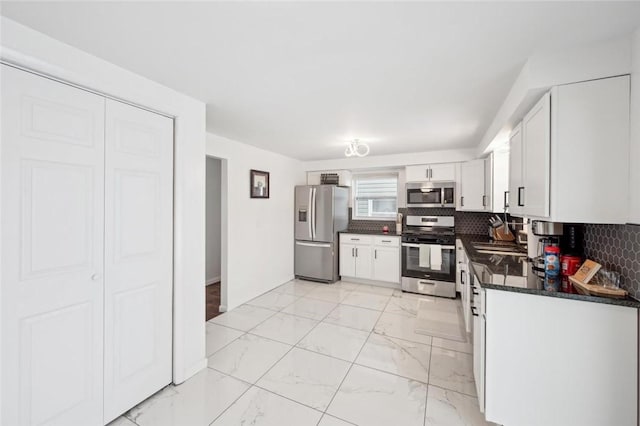 kitchen with sink, stainless steel appliances, tasteful backsplash, dark stone countertops, and white cabinets