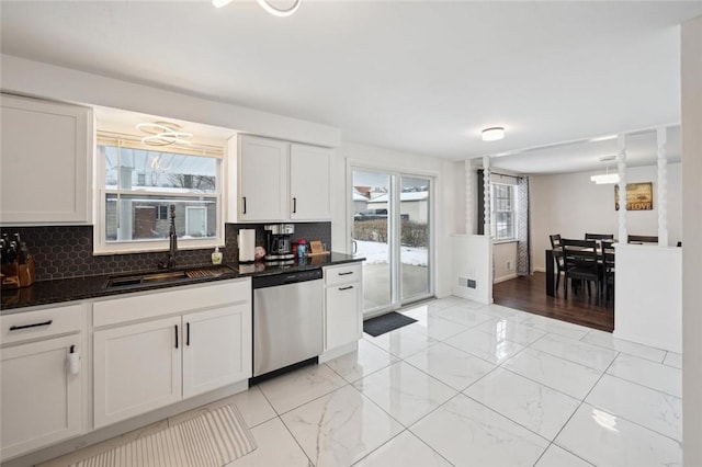 kitchen with sink, stainless steel dishwasher, dark stone countertops, tasteful backsplash, and white cabinetry