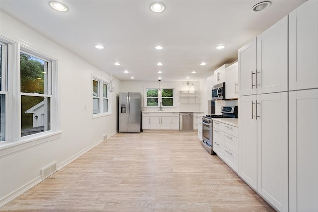 kitchen with appliances with stainless steel finishes, light hardwood / wood-style floors, sink, white cabinetry, and tasteful backsplash