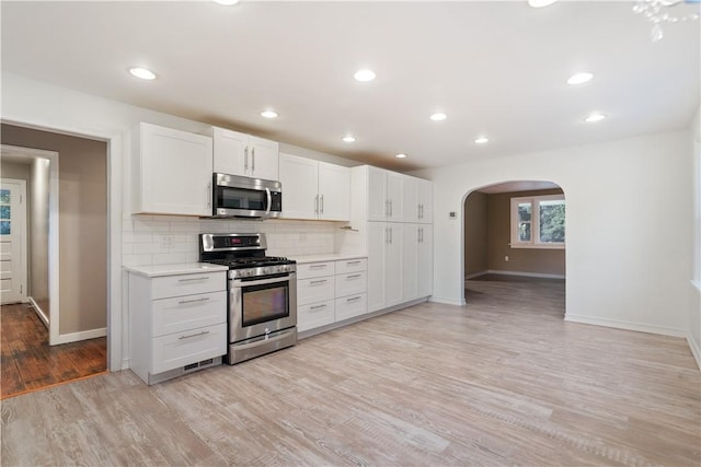 kitchen with appliances with stainless steel finishes, light wood-type flooring, white cabinets, and decorative backsplash