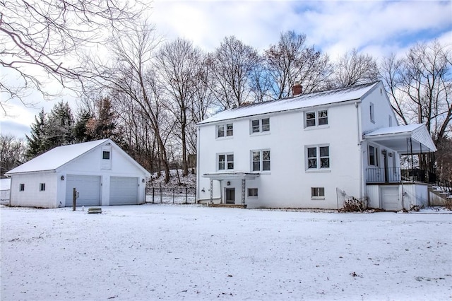 snow covered house featuring a porch, a garage, and an outdoor structure