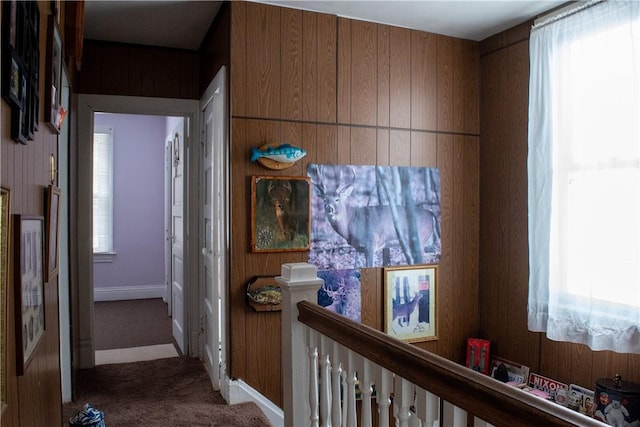 corridor with carpet floors, wood walls, and plenty of natural light