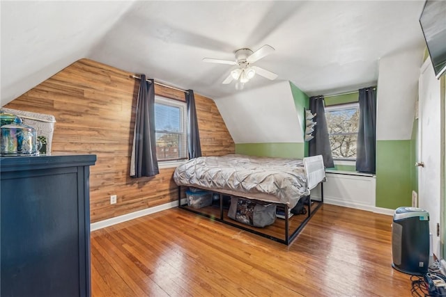 bedroom with lofted ceiling, ceiling fan, wood-type flooring, and wooden walls