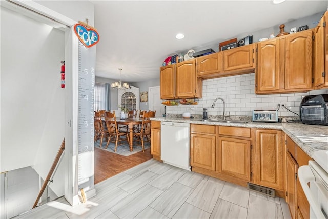 kitchen with a chandelier, white dishwasher, pendant lighting, sink, and tasteful backsplash