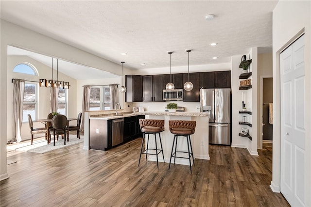 kitchen featuring vaulted ceiling, dark brown cabinets, hanging light fixtures, dark hardwood / wood-style flooring, and appliances with stainless steel finishes