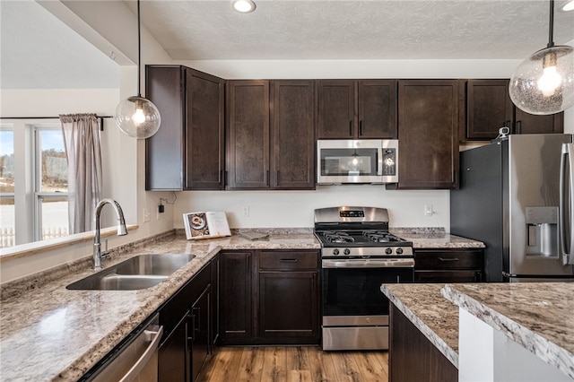 kitchen featuring stainless steel appliances, sink, light wood-type flooring, hanging light fixtures, and dark brown cabinetry