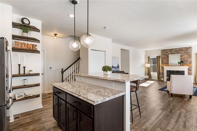 kitchen with decorative light fixtures, a center island, light stone counters, a brick fireplace, and dark brown cabinetry