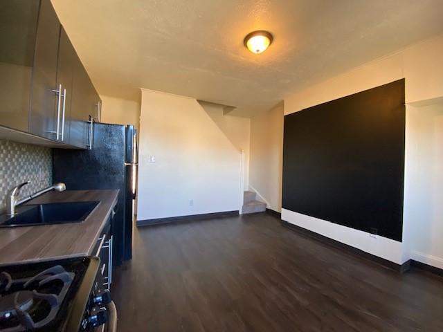 kitchen featuring tasteful backsplash, stainless steel gas range, baseboards, dark wood-style floors, and a sink