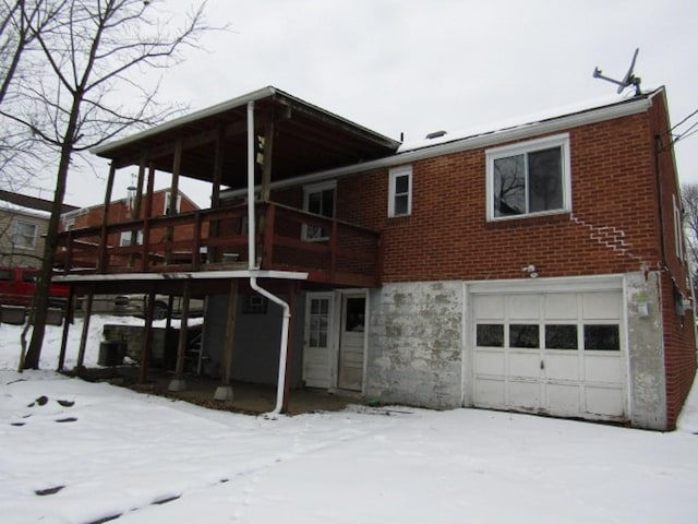 snow covered rear of property featuring a garage and a wooden deck