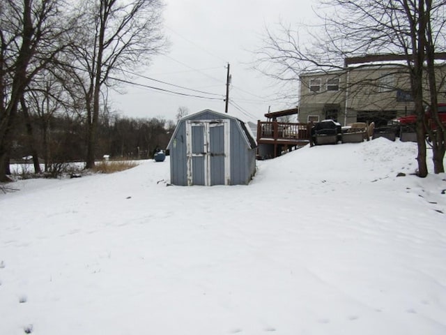 yard layered in snow with a wooden deck and a storage shed