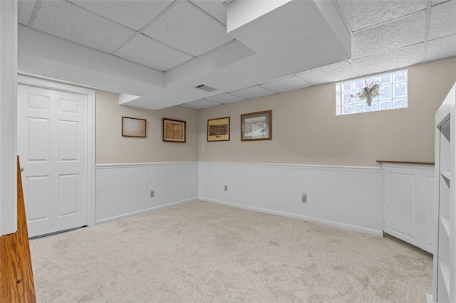 basement with a paneled ceiling and light colored carpet