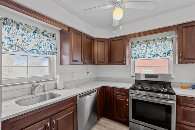 kitchen featuring stainless steel appliances, light wood-type flooring, ceiling fan, light stone counters, and sink