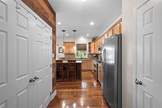 kitchen with appliances with stainless steel finishes, decorative light fixtures, a kitchen breakfast bar, tasteful backsplash, and dark wood-type flooring