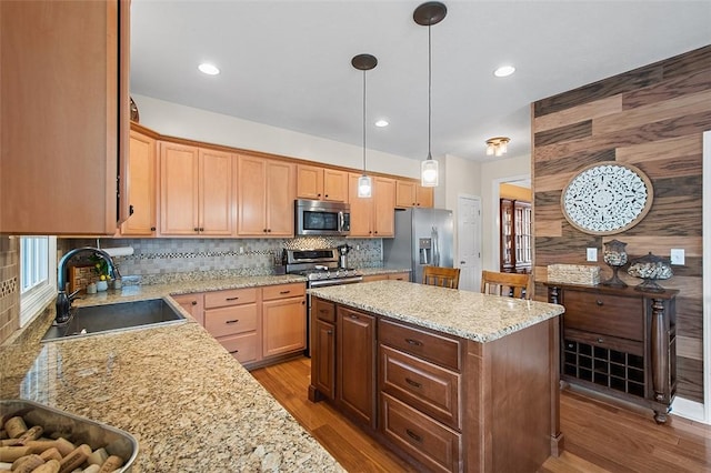 kitchen with light stone counters, pendant lighting, a center island, appliances with stainless steel finishes, and sink