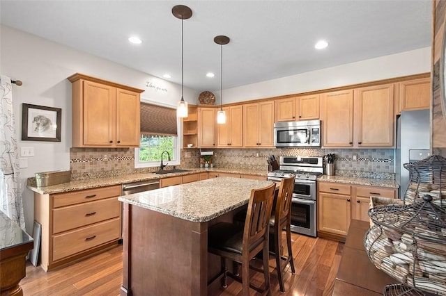 kitchen with stainless steel appliances, sink, light stone counters, light hardwood / wood-style flooring, and hanging light fixtures