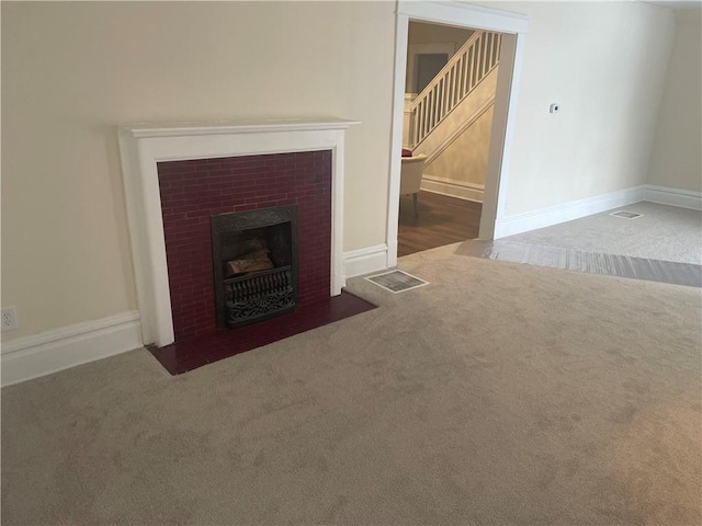 unfurnished living room featuring visible vents, baseboards, a fireplace with flush hearth, stairs, and carpet floors