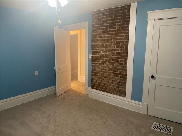 unfurnished bedroom featuring baseboards, brick wall, visible vents, carpet floors, and a closet