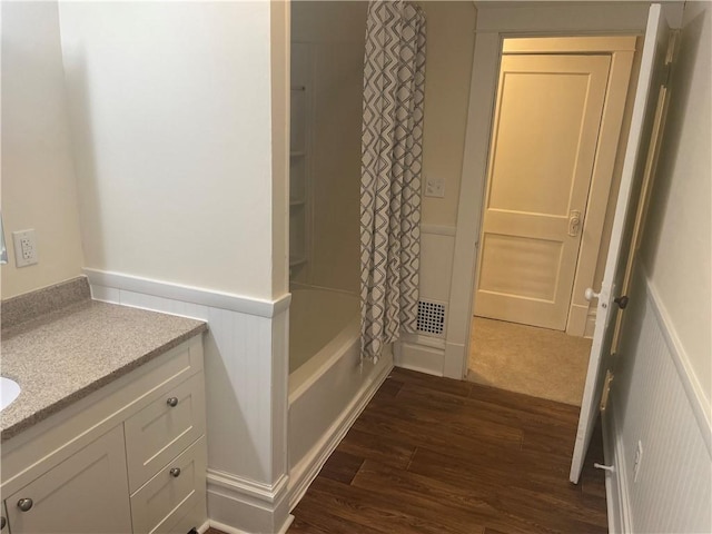 bathroom with a wainscoted wall, wood finished floors, a decorative wall, shower / bath combination with curtain, and vanity