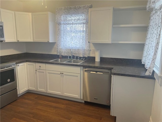 kitchen with dark countertops, dark wood finished floors, appliances with stainless steel finishes, white cabinets, and a sink