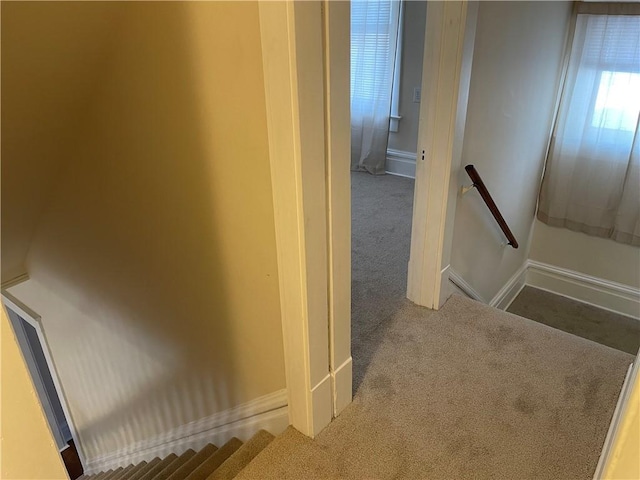 hallway with an upstairs landing, baseboards, and carpet