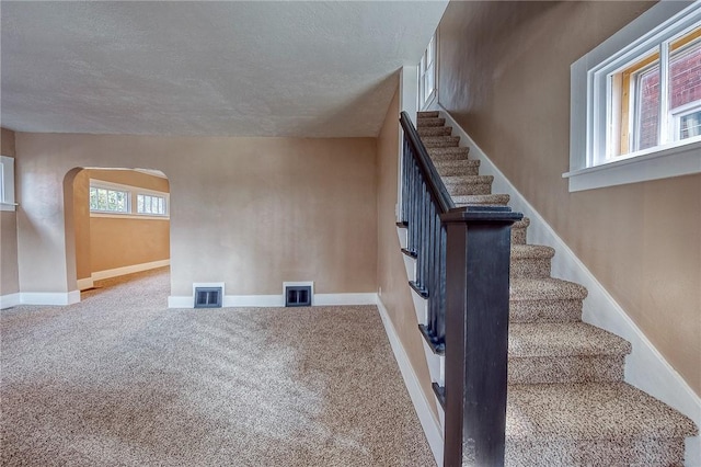 stairway with a textured ceiling and carpet