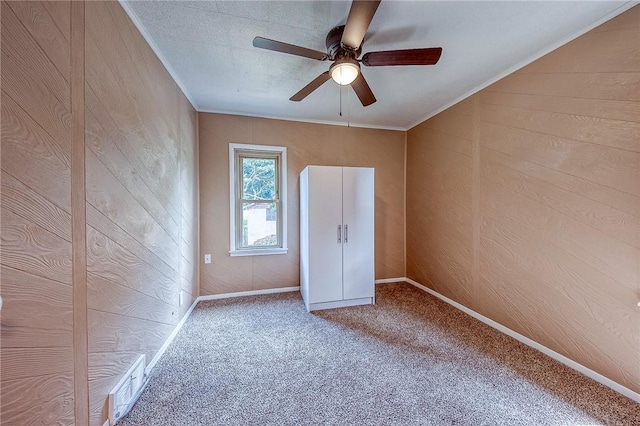 unfurnished room featuring ornamental molding, carpet flooring, ceiling fan, and wood walls