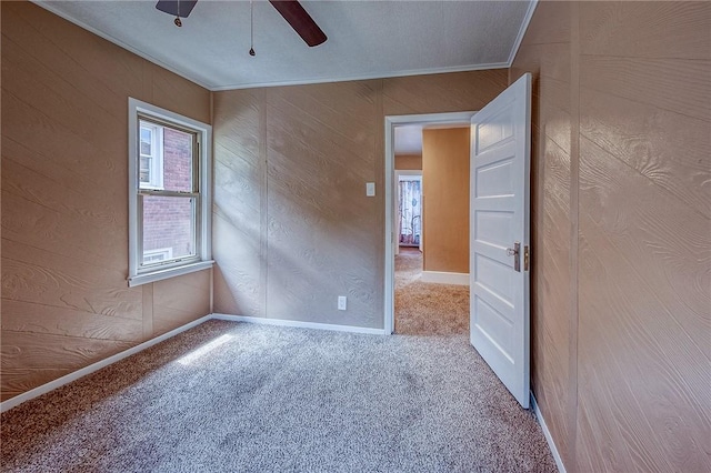 carpeted spare room featuring ceiling fan, ornamental molding, and wooden walls