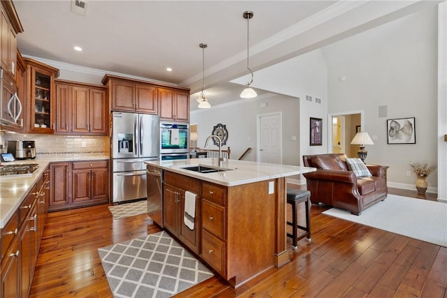 kitchen featuring a center island with sink, stainless steel appliances, decorative backsplash, sink, and decorative light fixtures