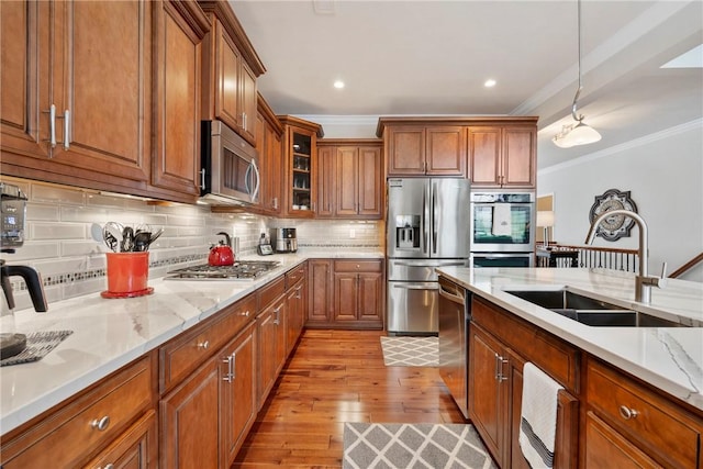 kitchen featuring stainless steel appliances, crown molding, sink, decorative light fixtures, and tasteful backsplash