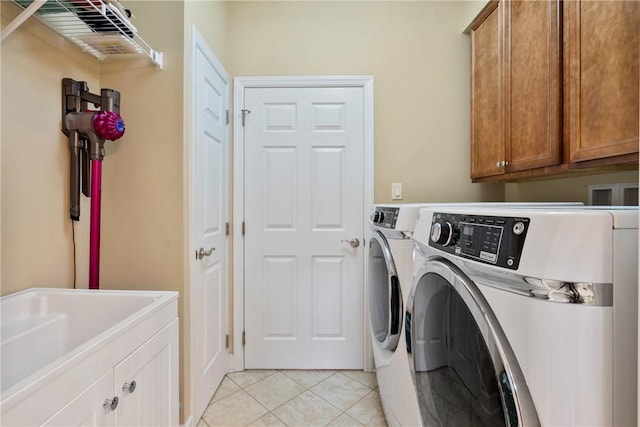 clothes washing area featuring sink, washing machine and dryer, light tile patterned floors, and cabinets