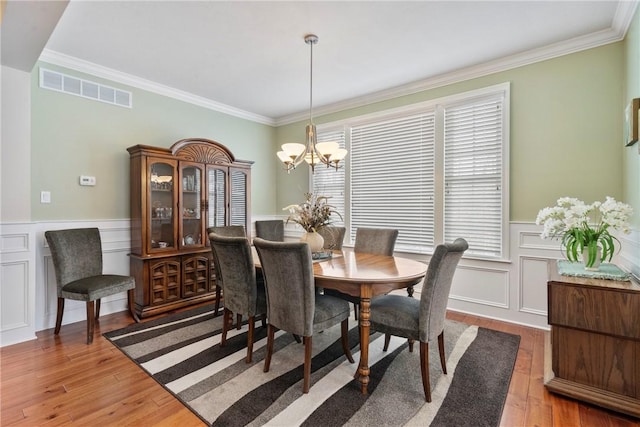 dining space featuring wood-type flooring, ornamental molding, and a chandelier