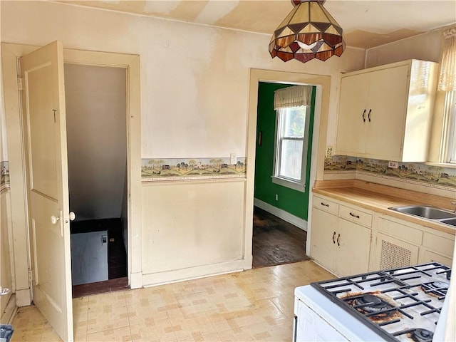 kitchen with sink, decorative light fixtures, white range with gas stovetop, and white cabinets