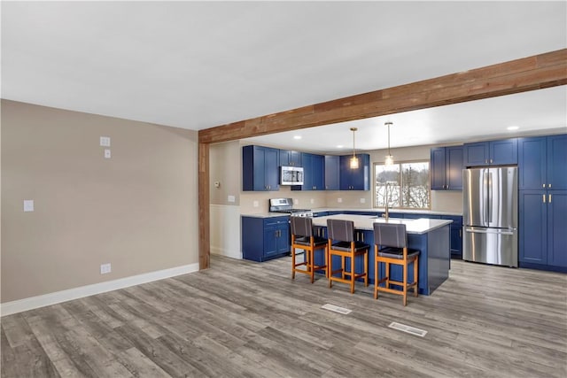 kitchen featuring light wood-type flooring, appliances with stainless steel finishes, a kitchen bar, and blue cabinetry