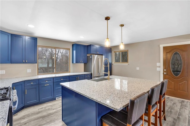 kitchen featuring a breakfast bar, light hardwood / wood-style flooring, light stone countertops, an island with sink, and stainless steel appliances